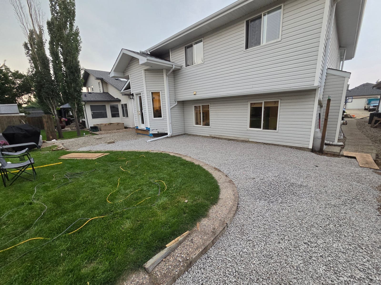 Compacted gravel yard behind a house, curving around a new lawn with a timber edge