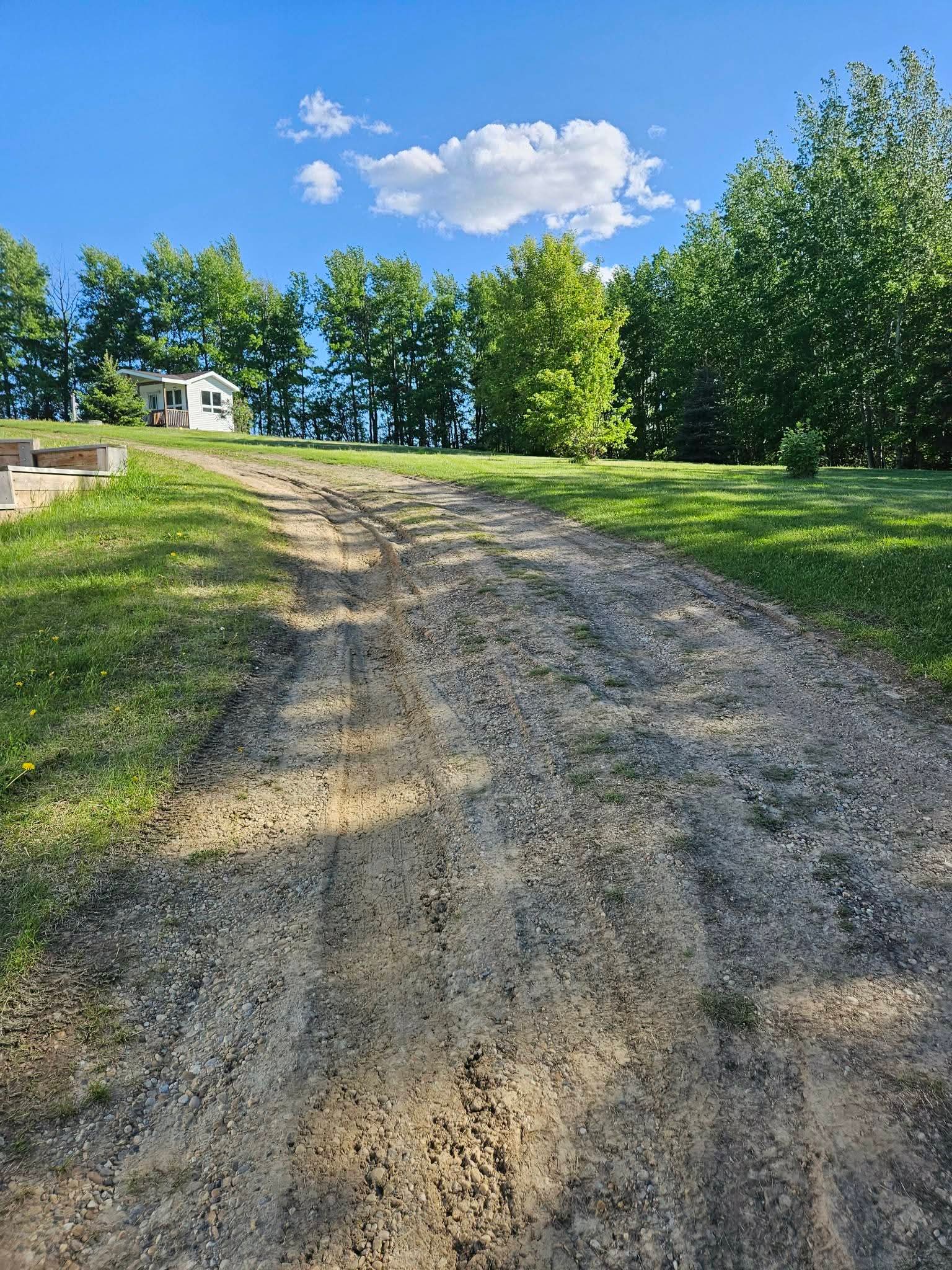 Rutted, washed-out dirt driveway running up a hill to a white house