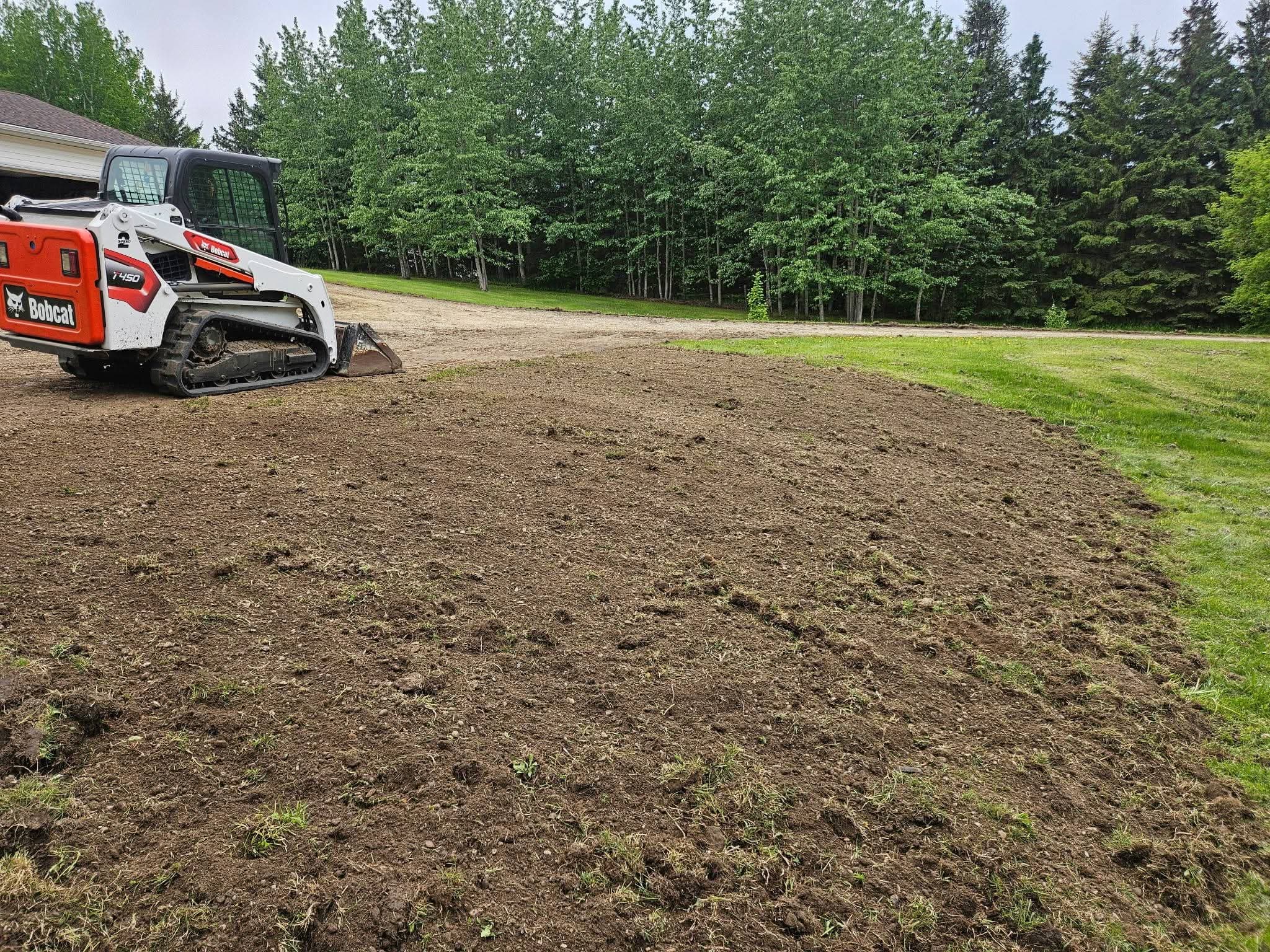 Bobcat T450 track loader levelling stripped ground beside a driveway