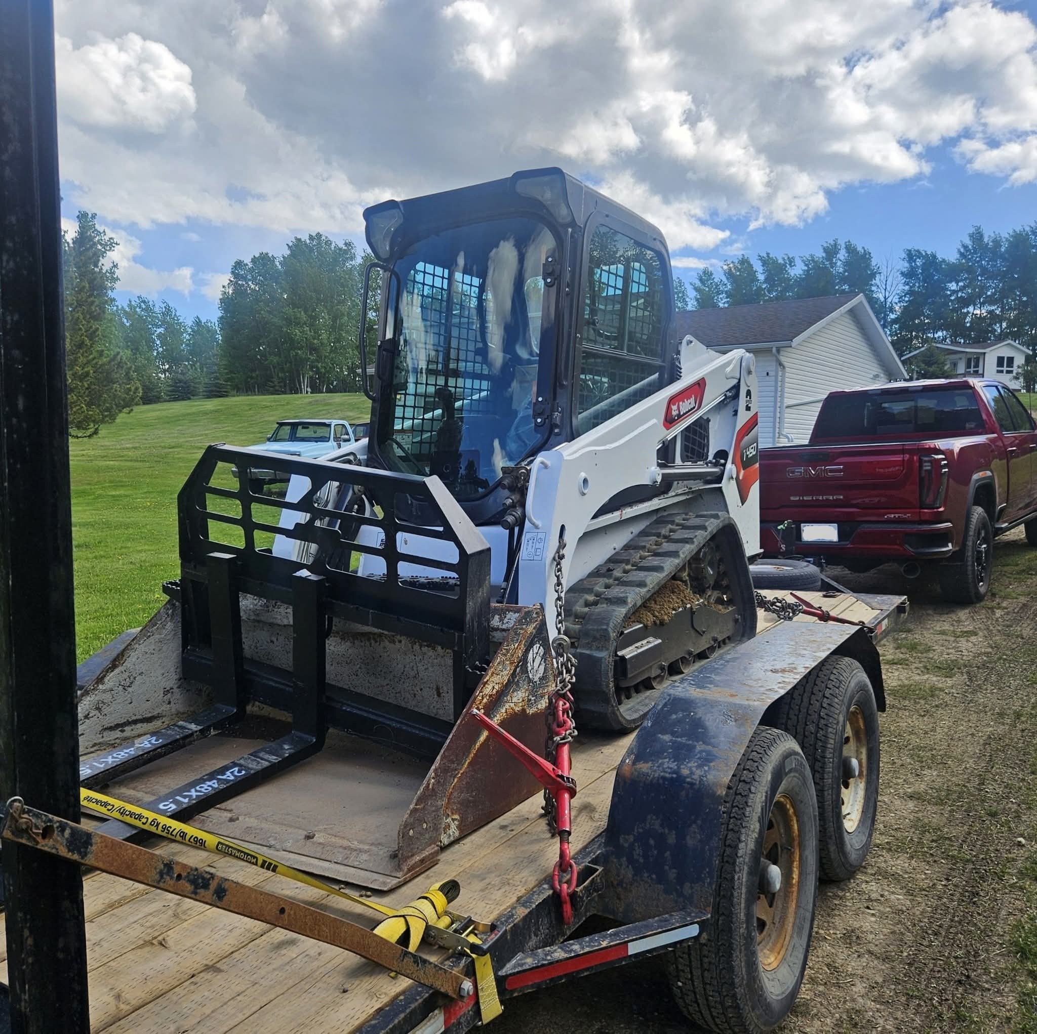 Bobcat T450 with pallet forks chained down on an equipment trailer