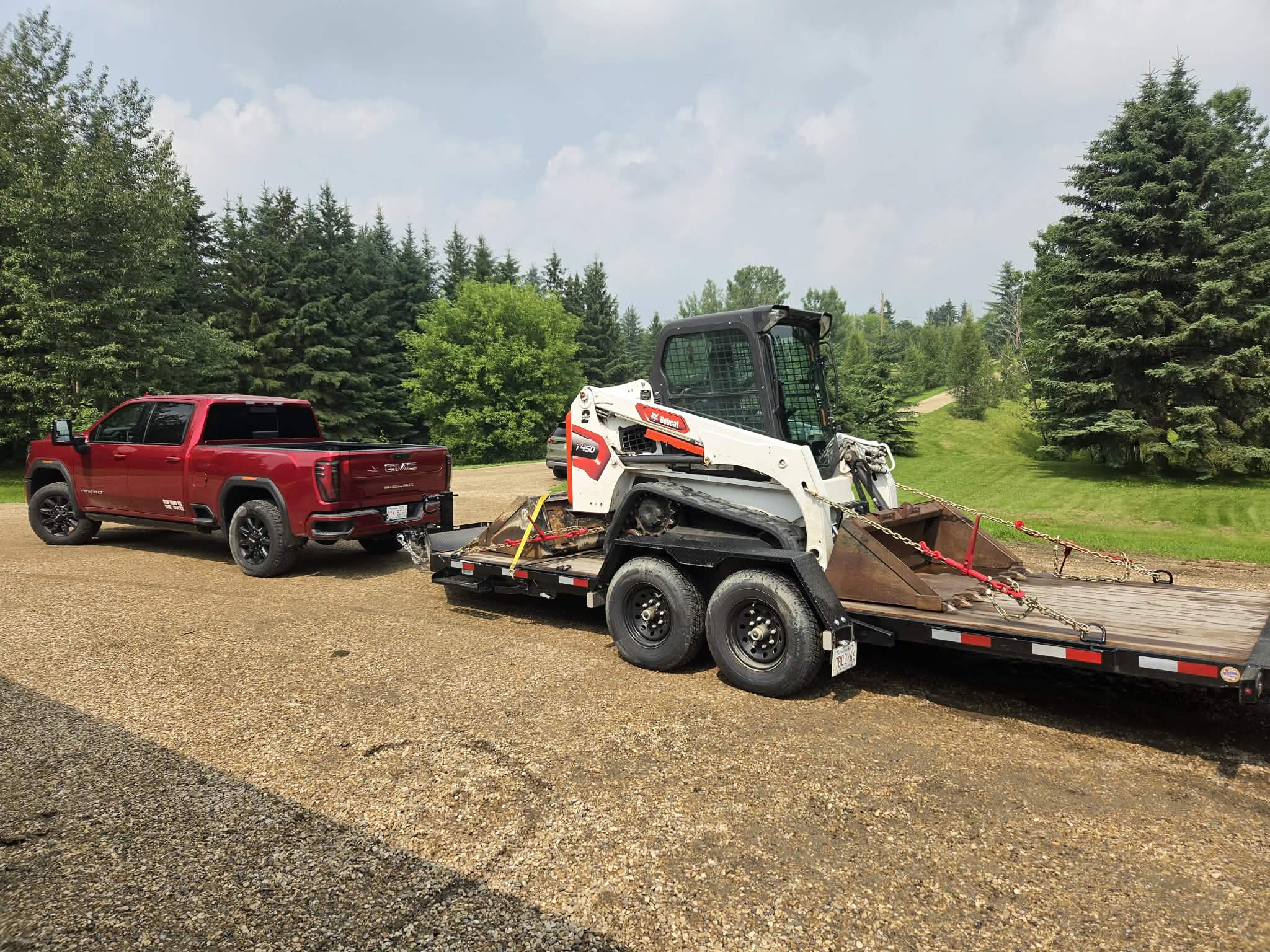 Red GMC Sierra and equipment trailer loaded with a Bobcat T450 track loader